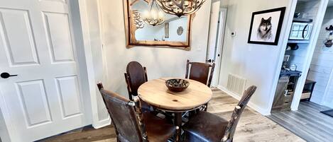 Une salle à manger avec une table ronde, quatre chaises, un lustre, un miroir et un tableau encadré accroché au mur.