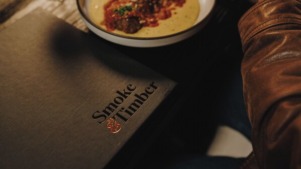 Un livre intitulé « Smoke & Timber » est posé sur une table, à côté d’une assiette de nourriture.