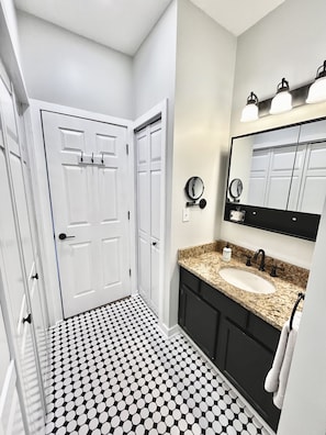 A bathroom with a white door, a sink with a granite countertop, a mirror, and a black and white patterned floor. - Escape to Mountain Paradise - 1BR/1BA Condo with Breathtaking Views of the Blue Ridge Mountains! (Mars Hill)