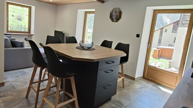 Una cocina moderna con una isla central, sillas negras y un sofá gris al fondo.
