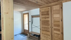 Una habitación con vigas de madera en el techo, un perchero metálico y suelo de baldosas.