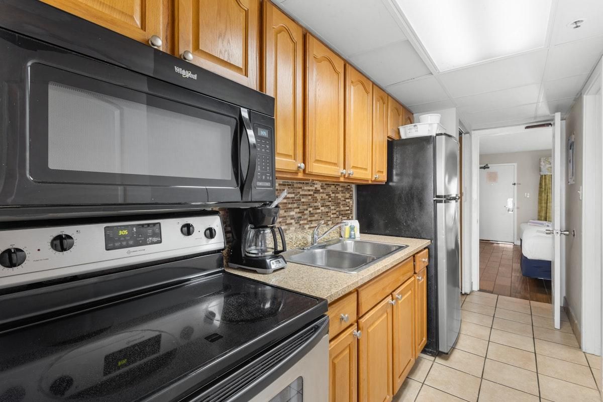 A kitchen with wooden cabinets, a black microwave, a stove, a refrigerator, and a coffee maker.