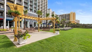 A hotel courtyard with a pergola, seating areas, and a grassy lawn.