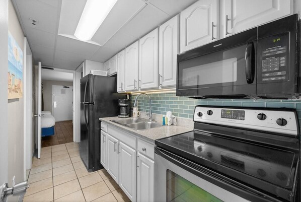 Une cuisine moderne avec des meubles blancs, un réfrigérateur noir, un four à micro-ondes et une cuisinière.