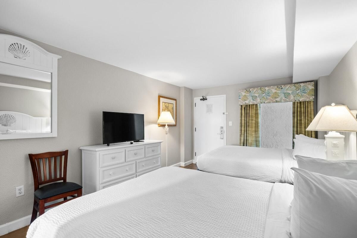 Una habitación de hotel con dos camas, televisión, escritorio con lámpara y una silla.