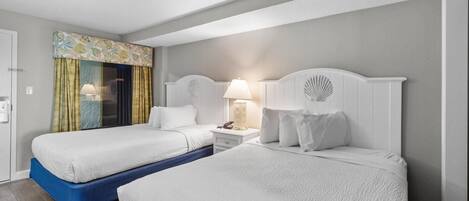 Habitació d'hotel amb dos llits, una finestra amb cortines, una tauleta de nit amb una làmpada i un panell decoratiu al capçal.