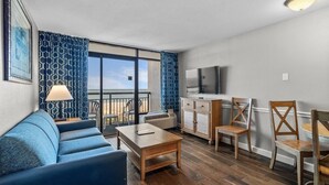 Un salon moderne avec un canapé, une table basse et un téléviseur. Il y a un balcon avec vue sur l’océan.