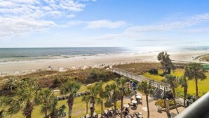 Une vue sur la plage avec un espace patio, des palmiers et une terrasse en bois donnant accès à la plage.