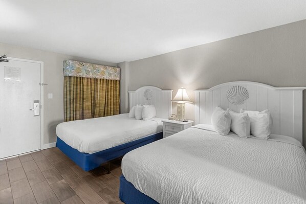 Une chambre d’hôtel avec deux lits, une porte, une table de chevet avec une lampe et un rideau.