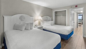A hotel room with two beds, a nightstand with a lamp, and a view of the beach through an open door. - Mesmerizing Oceanfront Ste 4th Flr w/ Breakfast (Myrtle Beach)