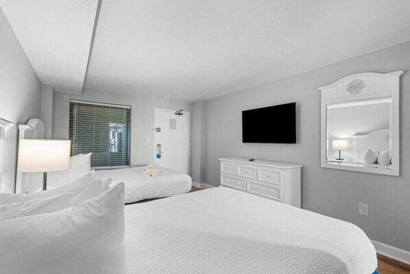 A hotel room with two beds, a flat-screen TV, a dresser, and a window with blinds. - Airy Oceanfront Suite 4th Flr with Breakfast (Myrtle Beach)