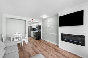 Una sala de estar moderna con un televisor de pantalla plana montado en la pared, un sofá gris y una zona de comedor con sillas blancas.