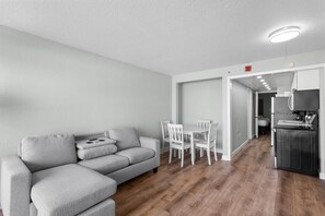 A modern living room with a grey sofa, a dining table with chairs, and a kitchen area with a refrigerator and microwave. - Airy Oceanfront Suite 4th Flr with Breakfast (Myrtle Beach)