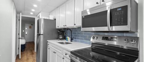 A modern kitchen with stainless steel appliances, white cabinets, and a tiled backsplash.