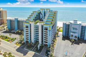 Hotel offers ocean views from its balconies, situated near a parking area and road.