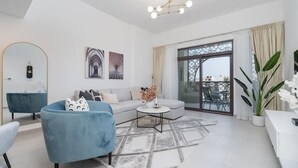 A modern living room with a sofa, armchair, and coffee table, a large window with a view, and a chandelier. - Vogue | Rahaal Madinat Jumeirah near Burj Al Arab (Dubai)
