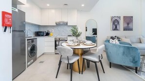 A modern kitchen with white cabinets, a stainless steel refrigerator, and a dining area with a round table and chairs. - Vogue | Rahaal Madinat Jumeirah near Burj Al Arab (Dubai)