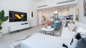 A modern living room with a flat-screen TV, a white sofa, a coffee table, and a kitchen in the background. - Vogue | Rahaal Madinat Jumeirah near Burj Al Arab (Dubai)