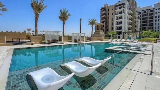 A swimming pool with lounge chairs, palm trees, and modern buildings in the background. - Vogue | Rahaal Madinat Jumeirah near Burj Al Arab (Dubai)
