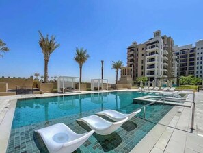 A swimming pool with lounge chairs, palm trees, and modern buildings in the background. - Vogue | Rahaal Madinat Jumeirah near Burj Al Arab (Dubai)
