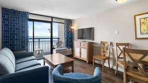 A modern living room with a sofa, chairs, a TV, and a dining table. - Inspiring Oceanfront Suite w/Free Breakfast 5th Flr (Myrtle Beach)