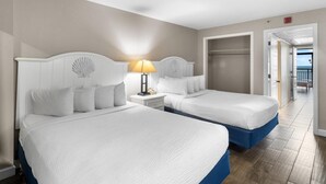 A hotel room with two beds, a nightstand with a lamp, and a view of the beach through an open door. - Inspiring Oceanfront Suite w/Free Breakfast 5th Flr (Myrtle Beach)