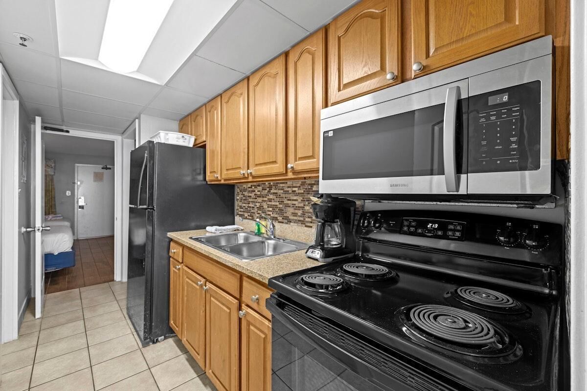 A modern kitchen with wooden cabinets, a stainless steel microwave, a black refrigerator, a double oven, and a granite countertop.