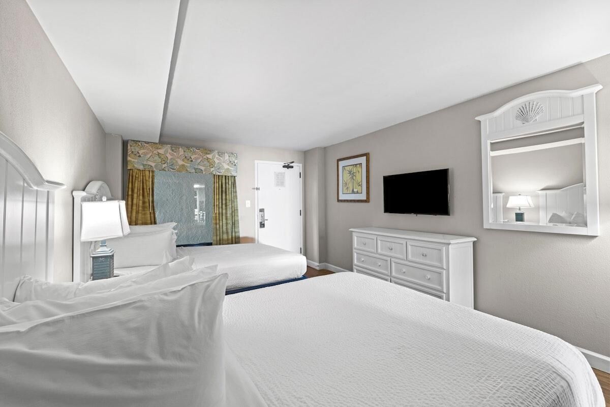 Una habitación de hotel con dos camas, un televisor, un aparador y una puerta que da a un baño.
