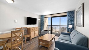 A modern living room with a wooden dining table, chairs, a sofa, and a TV mounted on the wall. - Beachy Oceanfront Suite 5th Flr With Breakfast (Myrtle Beach)