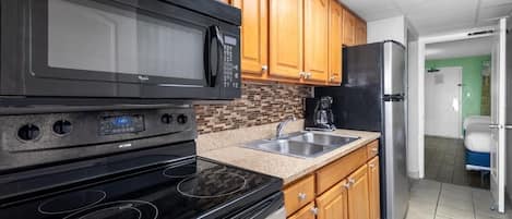 Una cocina con armarios de madera, un microondas negro, una estufa y un refrigerador.