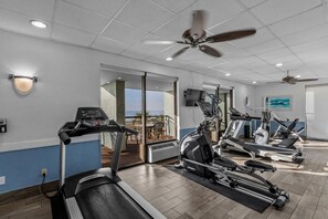 Uma academia com esteiras, elípticos e um ventilador de teto.