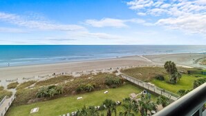 Uitzicht op het strand vanaf een balkon met een gazon, palmbomen en een houten terras.