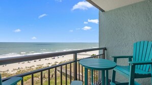 A balcony with a view of the beach, a small table, and two chairs.