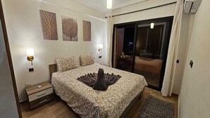 A hotel room with a large bed, a nightstand, a lamp, and a view of the city through a sliding glass door. -  Bitty Apartment in the heart of gueliz with swimming pool (Marrakech)
