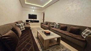 A modern living room with two sofas, a coffee table, and a flat-screen TV mounted on the wall. -  Bitty Apartment in the heart of gueliz with swimming pool (Marrakech)