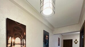 A hallway with a tiled floor, a hanging light fixture, and two framed artworks on the walls. -  Bitty Apartment in the heart of gueliz with swimming pool (Marrakech)