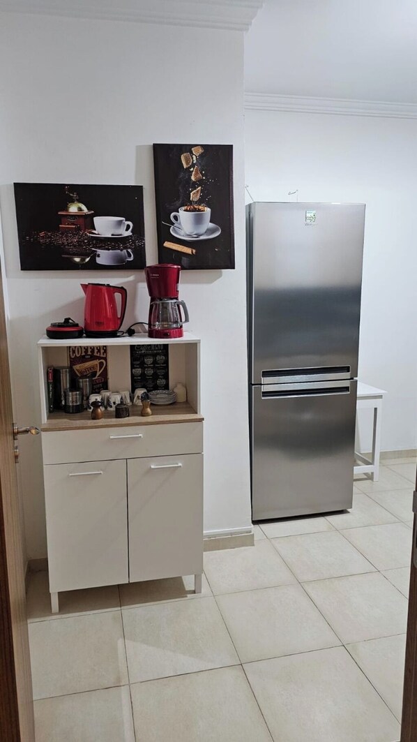 A kitchen with a stainless steel refrigerator, a coffee maker, and two framed pictures on the wall.