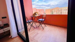 A balcony with a table and chairs, a window with curtains, and a view of buildings. -  Bitty Apartment in the heart of gueliz with swimming pool (Marrakech)