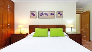 Ein Hotelzimmer mit einem großen Bett, zwei grünen Kissen, einem Holzschrank und drei an der Wand befestigten Blumenbildern.