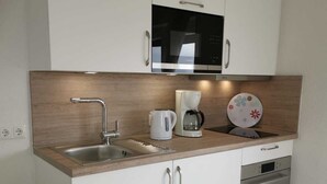 Una cucina moderna con mobili bianchi, un lavello in acciaio inossidabile, un forno a microonde, una macchina per il caffè e un tostapane.