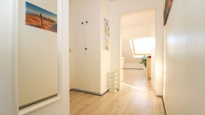 Un corridoio con pavimento in legno, pareti bianche e una porta decorata con un dipinto di un paesaggio.
