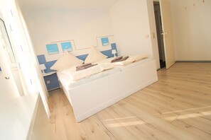 Un dormitorio con cama, suelo de madera y una puerta que da a otra habitación.