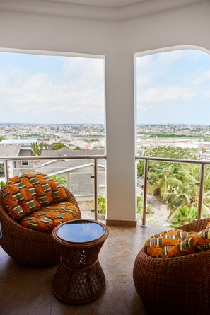 A balcony with wicker furniture and a view of a cityscape. - Enjoy a delightful stay in our Luxury 8 ensuite bedrooms with a stunning view (Accra)