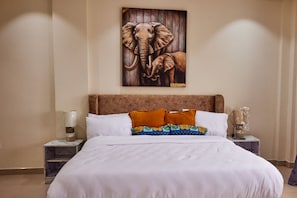 A hotel room with a large bed, white bedding, a wooden headboard, and a painting of an elephant on the wall. - Enjoy a delightful stay in our Luxury 8 ensuite bedrooms with a stunning view (Accra)