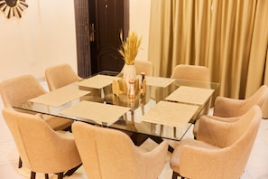 A modern dining area with a glass table surrounded by beige chairs, a vase with dried plants, and a decorative wall clock. - Enjoy a delightful stay in our Luxury 8 ensuite bedrooms with a stunning view (Accra)