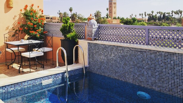 A rooftop pool with blue mosaic tiles, a table with chairs, and a potted plant. - Riad Beni Sidel (Marrakech)