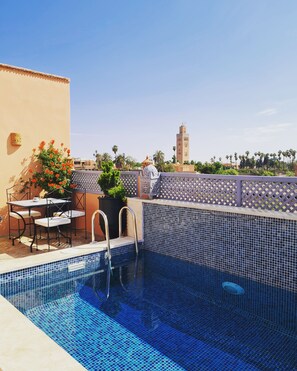 A rooftop pool with blue mosaic tiles, a table with chairs, and a potted plant. - Riad Beni Sidel (Marrakech)
