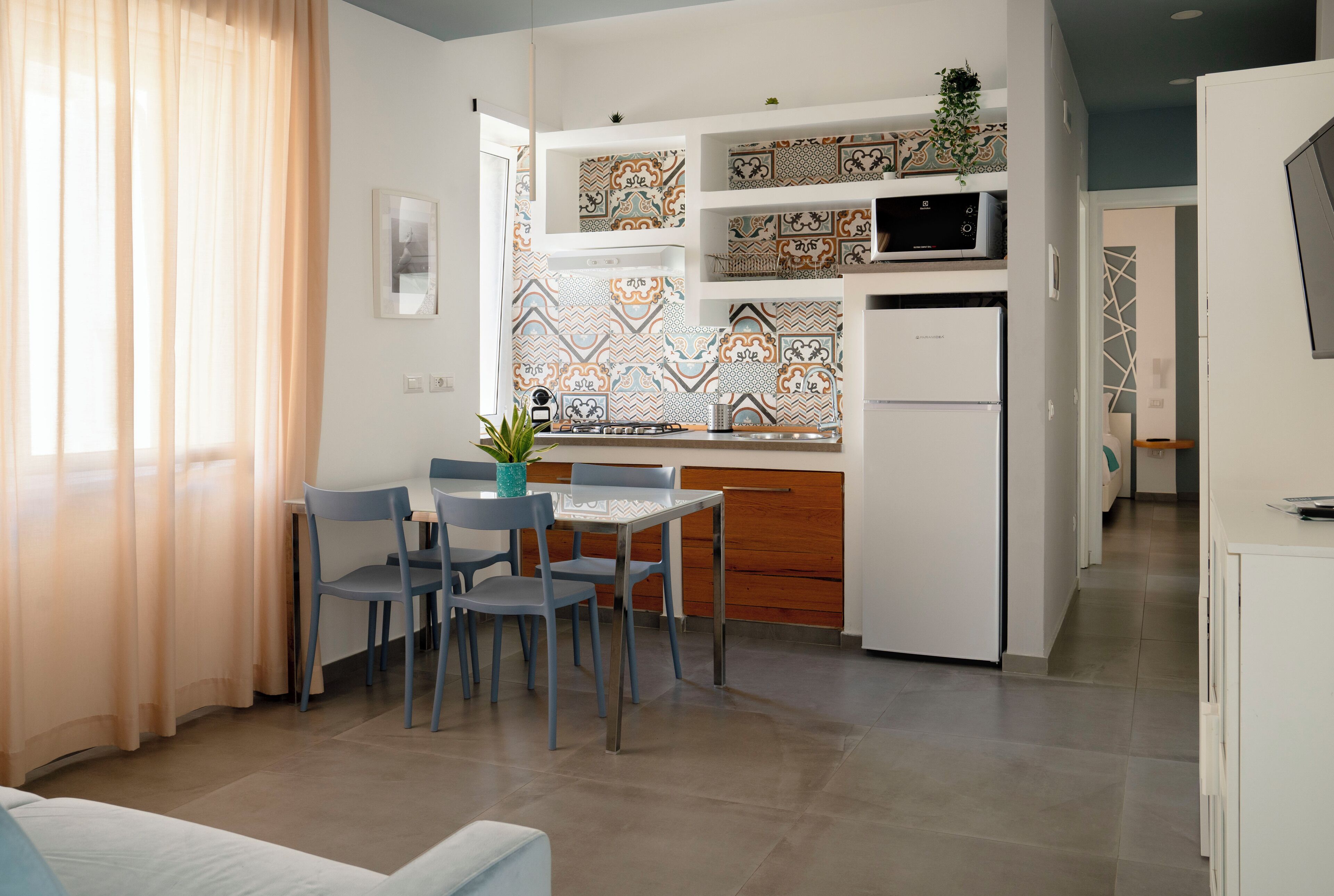 Une cuisine compacte avec un coin repas, dotée d’un design moderne, de crédences décorées de motifs, d’un four à micro-ondes et d’un réfrigérateur.