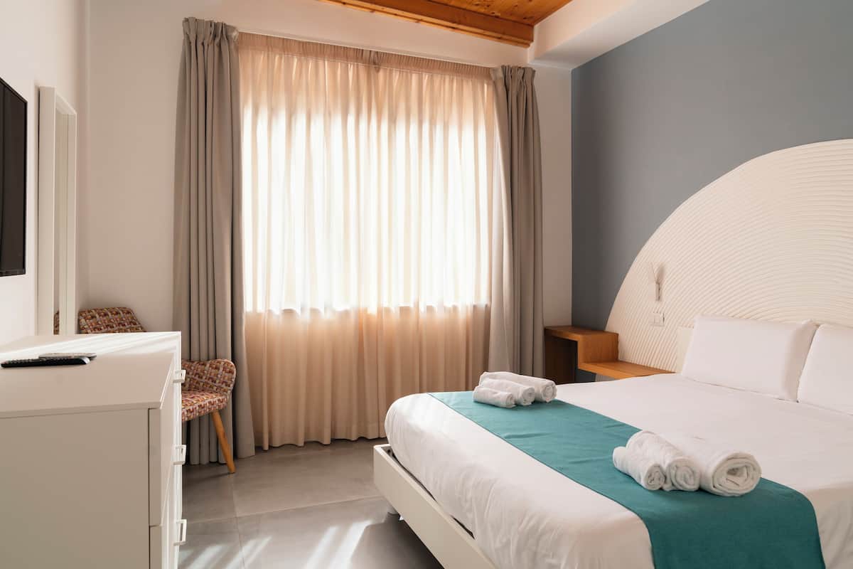 A hotel room with a bed, a desk, a chair, and a TV.