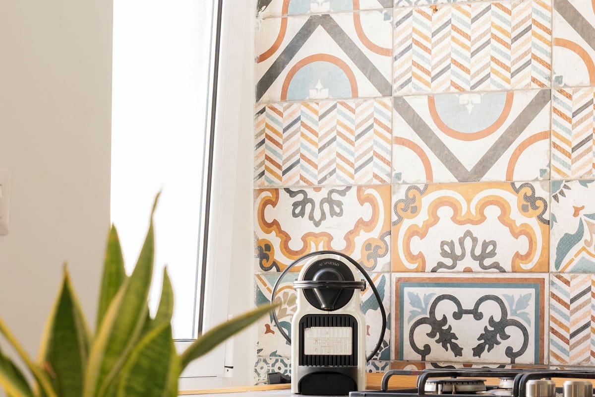 A kitchen with a coffee maker, a potted plant, and a window with patterned tiles.